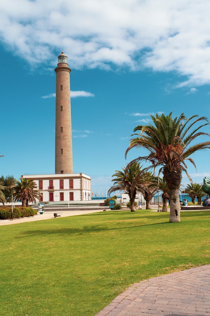 A stunning lighthouse on Gran Canaria amidst lush palm trees and bright skies.