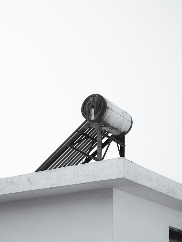A minimalist view of an urban rooftop featuring a solar water heater against a clear sky.