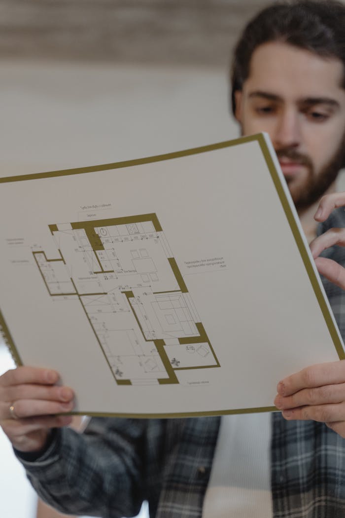 A man examines a detailed floor plan for a construction project indoors.